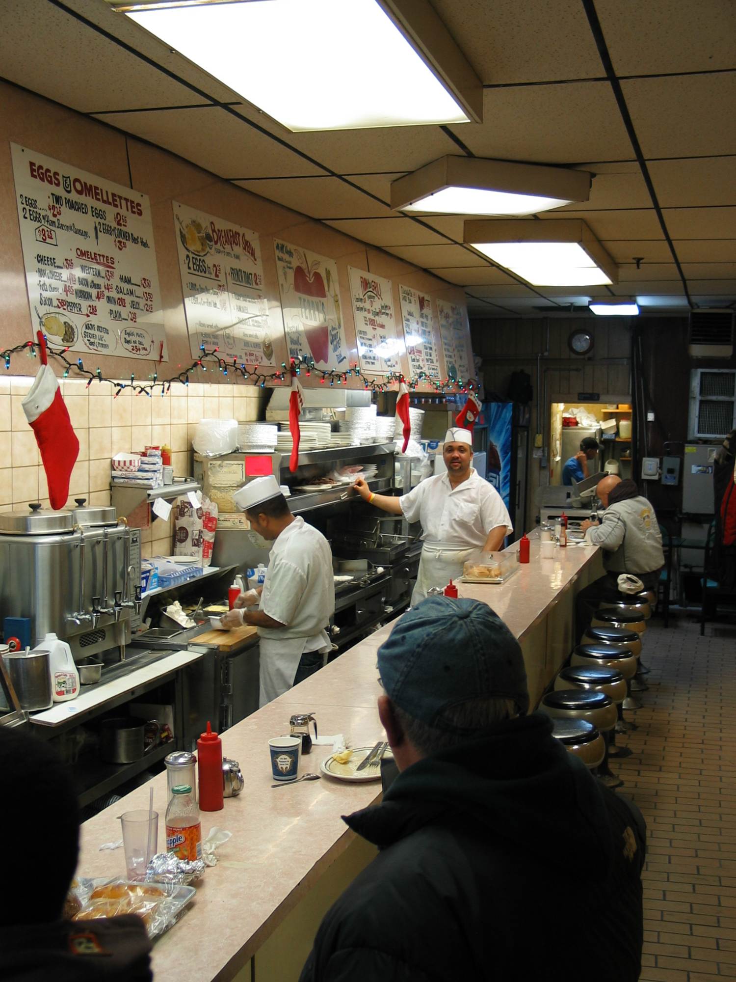 A classic American diner counter with cooks in whites and hand-painted menu boards
