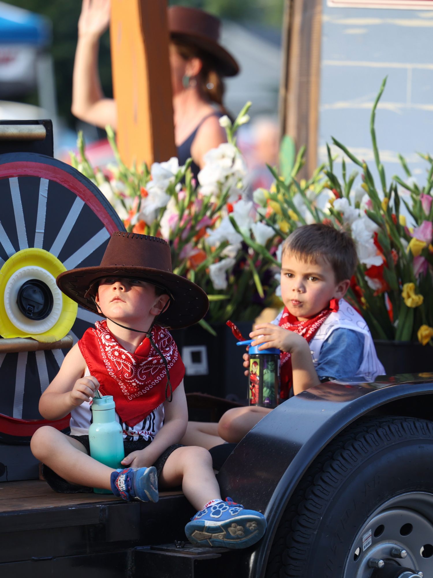 Children in cowboy hats and red bandanas ride a parade float stacked with gladioli